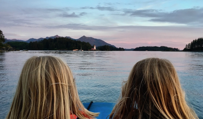 Two younf traveling kids posing near water at sunset