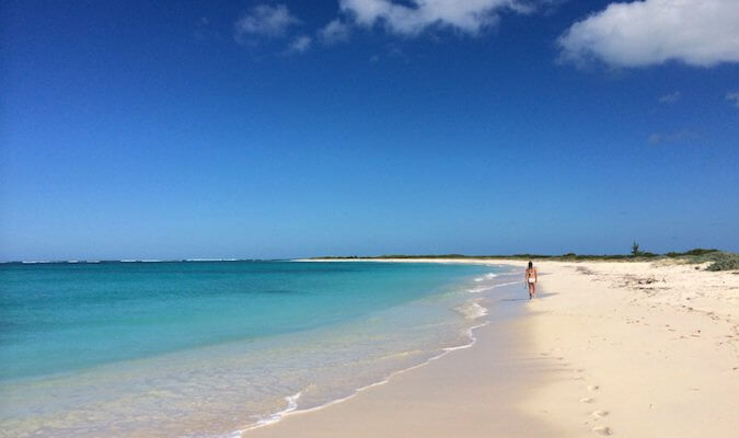 A woman walking down a deserted white sand beach in the BVIs