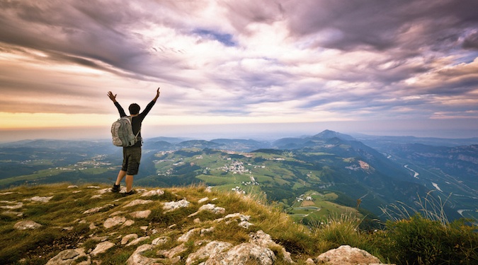 A solo traveler hiking, standing on the top of a mountain