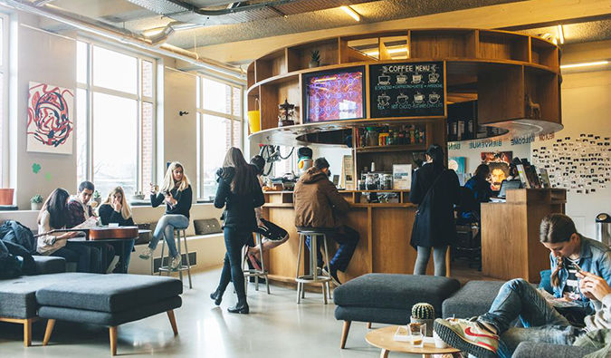 Common area with people sitting around on couches and at the circular coffee bar at Clink Noord