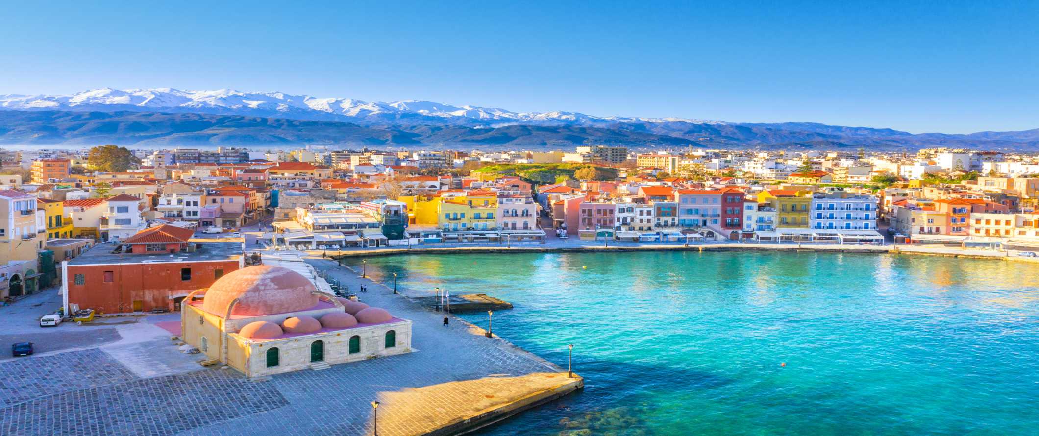 Aerial view of Chania with brightly colored houses on the harborfront and mountains in the background on the island of Crete in Greece