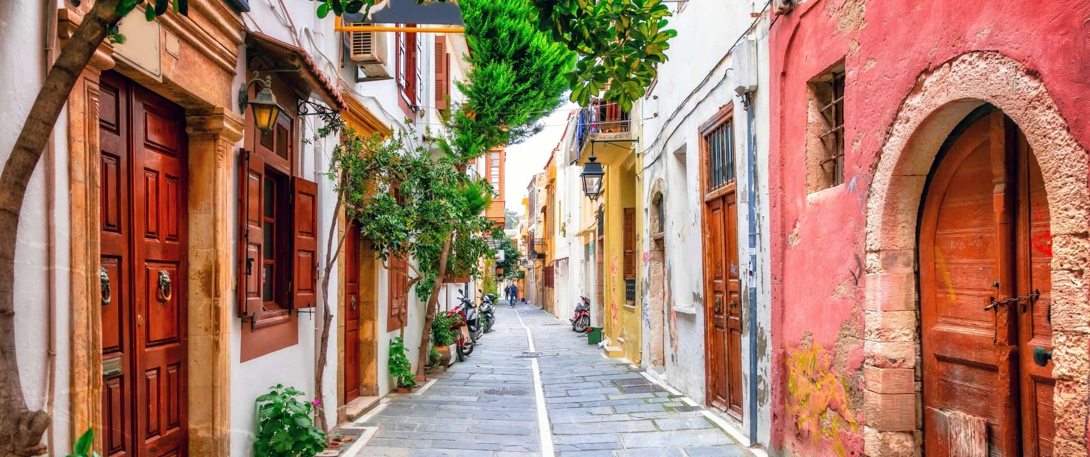 Flagstone-lined street flanked by brightly colored houses with wooden doorways on the island of Crete in Greece.