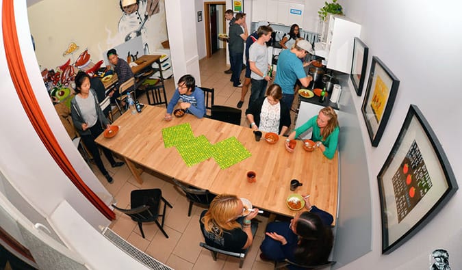 Fisheye style photo of kitchen at Hostel One in Prague, with people sitting at a table, preparing food, eating, and talking.