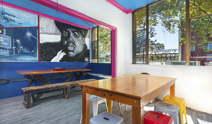 Common area with wooden tables, bright stools, and murals on the wall at Hump Backpackers hostel in Sydney, Australia