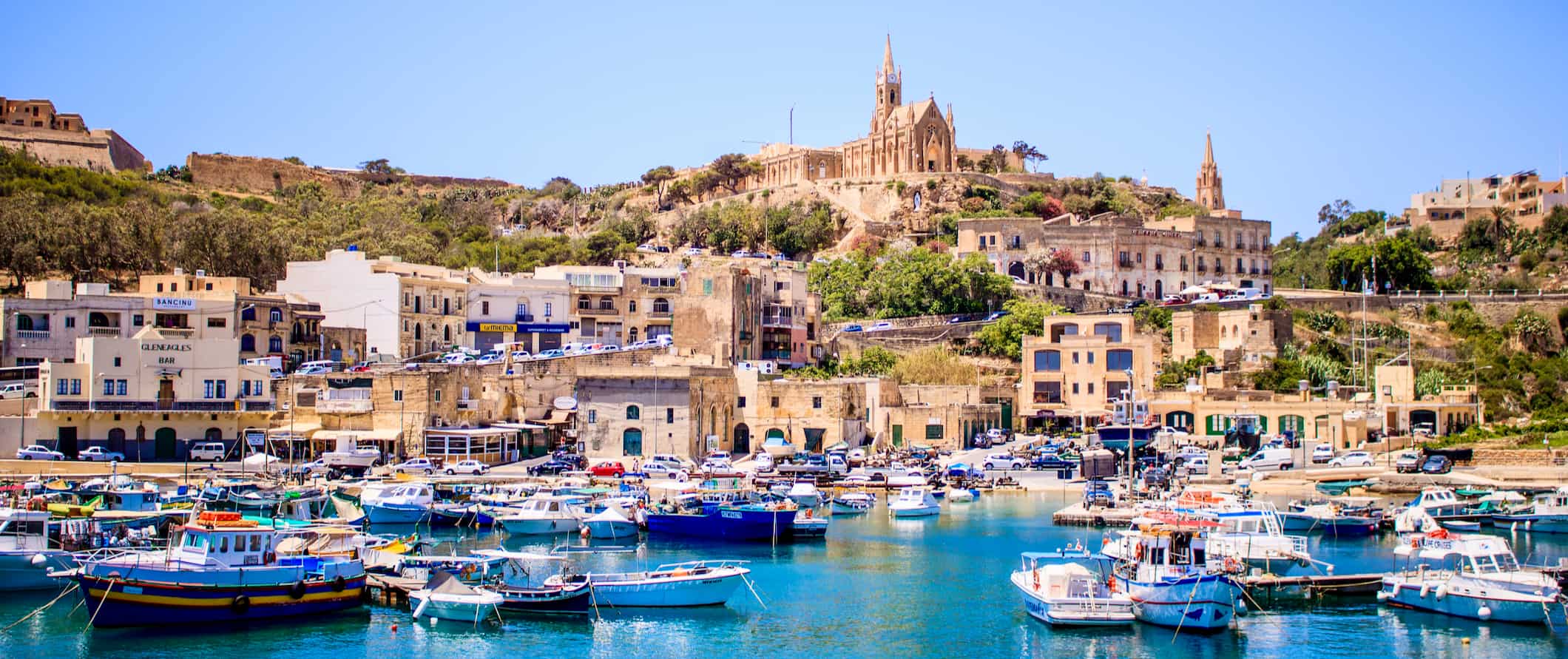 a view of the coast in Malta, lined by towering historic buildings near the harbor