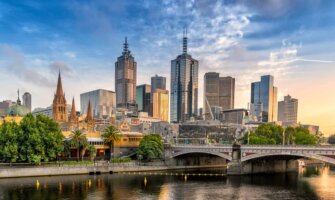 The towering skyline of Melbourne, Australia with trees and a bridge in the foreground near the river