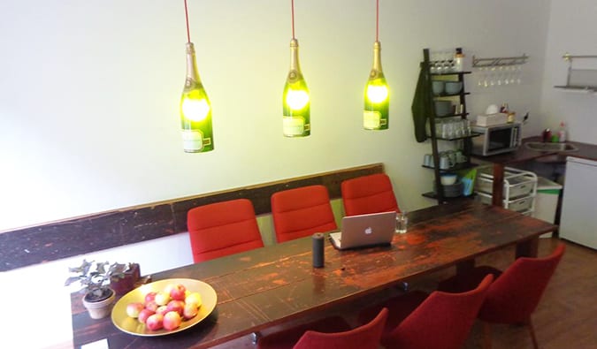 Kitchen area with long wooden table and hanging lamps made of wine bottles at Minimal Hostel Berlin, Berlin