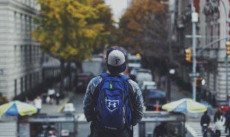 a man wearing a baseball cap and a blue backpack looks out onto a busy street from above