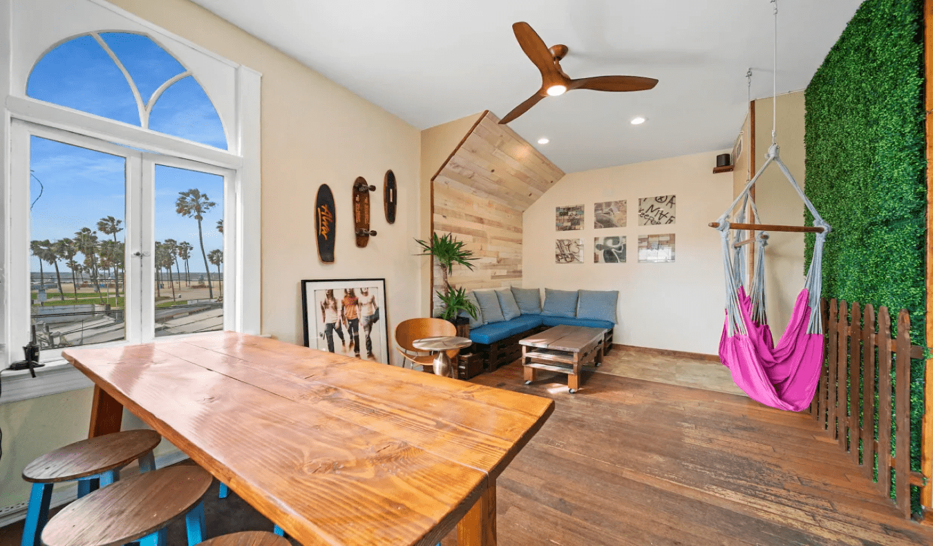 Common room with long wooden table, hammock, and couches at Samesun Venice Beach in Los Angeles.