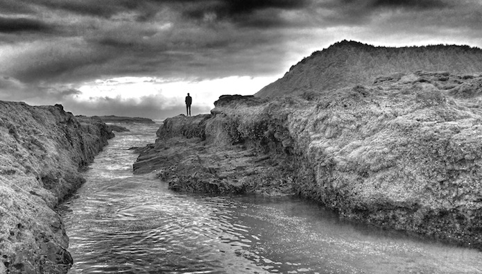 A black and white photo of a main on the ocean shore