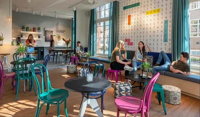 People hanging out in common area with circular tables and bright chairs at StayOkay Amsterdam Vondelpark