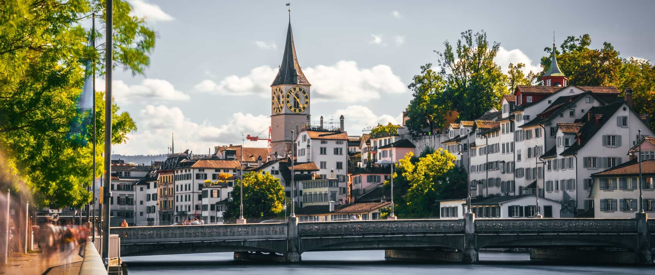 Historic buildings lining the waterfront and a large historic clocktower in the center in the Old Town of Zurich, Switzerland